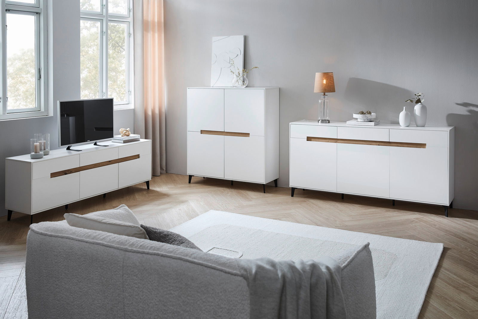 Wohnzimmer mit modernem weißen Sideboard, Highboard und TV-Lowboard in Frontalansicht, dekoriert mit Lampen und Vasen.