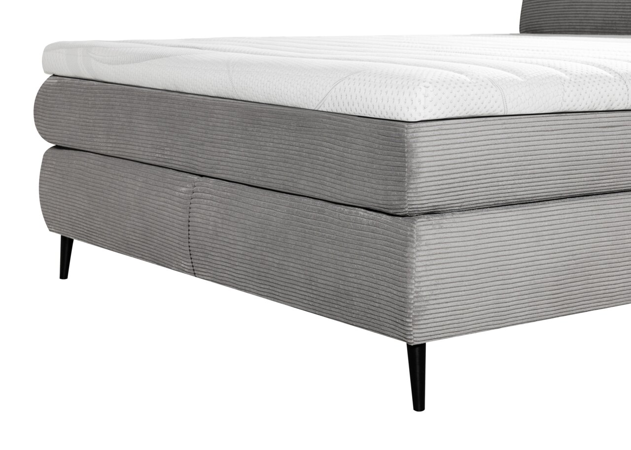 Zijaanzicht van een grijs boxspringbed met zwarte poten en een wit matras.