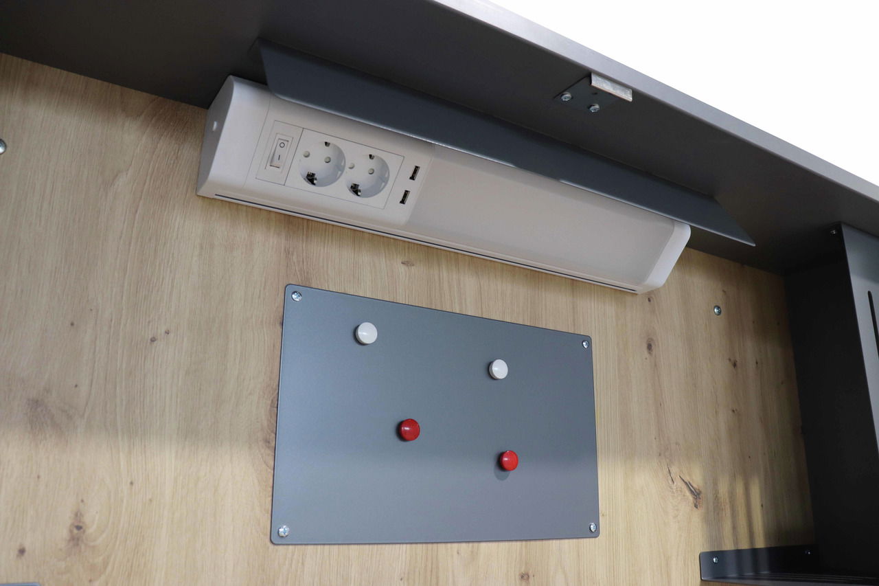 Nahaufnahme eines Wandschreibtischs mit Steckdosenleiste und grauer Magnettafel, Perspektive von unten.