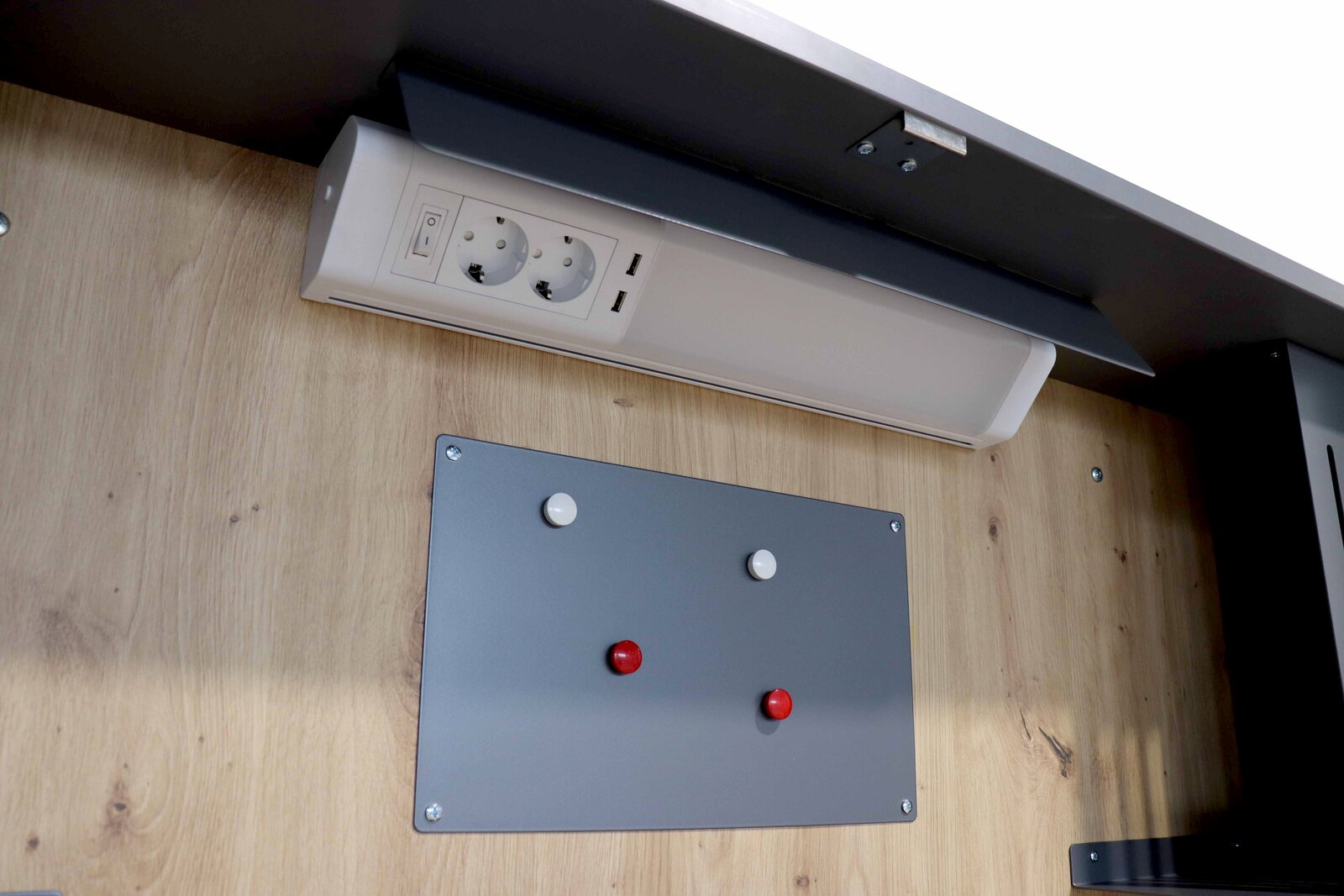 Nahaufnahme eines Wandschreibtischs mit Steckdosenleiste und grauer Magnettafel, Perspektive von unten.