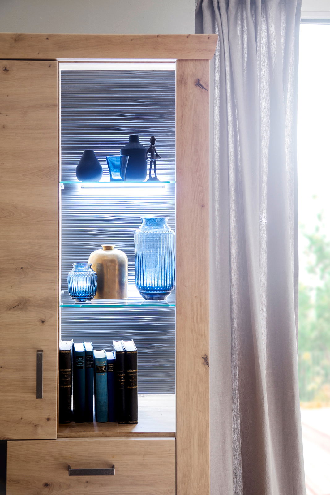 Detailansicht einer modernen Wandkombination mit LED-Beleuchtung, dekoriert mit blauen und goldenen Vasen sowie Büchern, von der Seite betrachtet.