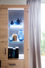 Detailansicht einer modernen Wandkombination mit LED-Beleuchtung, dekoriert mit blauen und goldenen Vasen sowie Büchern, von der Seite betrachtet.