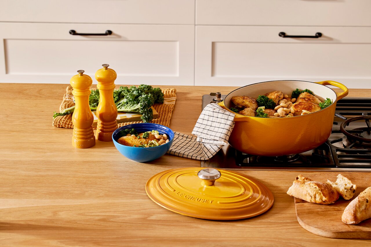 LE CREUSET Salzmühle Nectar Gelbe Salzmühle auf einem Holztisch in einer Küche, neben einer gelben Kasserolle mit Hähnchen und Bohnen, aus der Vogelperspektive.