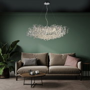 Moderne kroonluchter RICICLE in een stijlvolle woonkamer, gezien vanaf de voorkant, met een elegante bank en een groene muur op de achtergrond.
