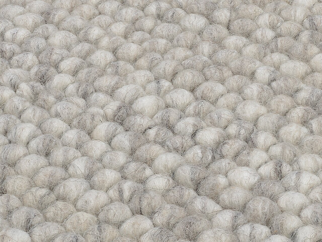 Nahaufnahme eines handgewebten Teppichs mit einer strukturierten, wolligen Oberfläche in natürlichen Grautönen.