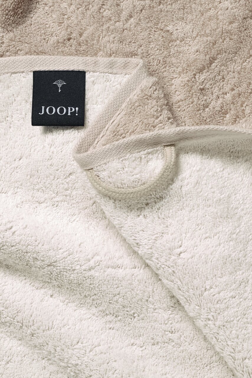 JOOP! Handdoek DOUBLEFACE CLASSIC Nahaufnahme eines beigen Duschtuchs mit einem schwarzen Etikett der Marke JOOP! in der Ecke.