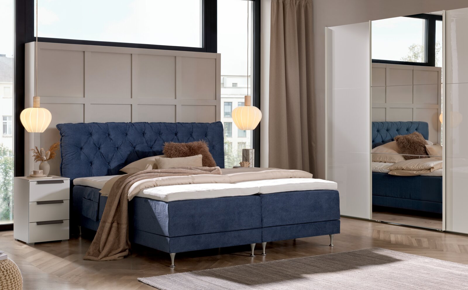 Blaues Boxspringbett mit gepolstertem, gestepptem Kopfteil und Metallfüßen in modernem Schlafzimmer, Frontansicht leicht schräg von vorn links