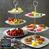 Zwei dreistufige, runde Etageren aus weißem Porzellan, gefüllt mit frischem Obst und bunten Macarons, seitliche Perspektive.