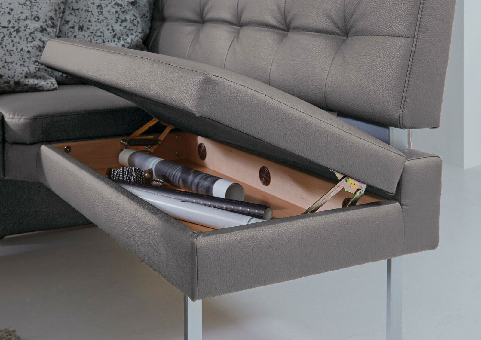 Nahaufnahme einer grauen Eckbank mit aufklappbarem Sitz, der Stauraum für Gegenstände bietet.