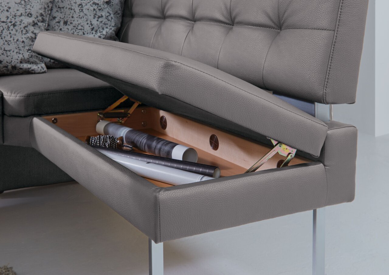 Nahaufnahme einer grauen Eckbank mit aufklappbarem Sitz, der Stauraum für Gegenstände bietet.