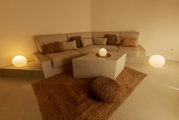 Gezellige, minimalistische zithoek met een beige hoekbank en kussens, een kubusvormige salontafel, een jute tapijt en een ronde staande lamp met warm licht, gefotografeerd vanuit een licht verhoogd vooraanzicht.