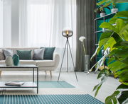 Moderne Stehleuchte MAXY mit dreibeinigem Stativ und kugelförmigem Lampenschirm in einem stilvollen Wohnzimmer, seitliche Perspektive.