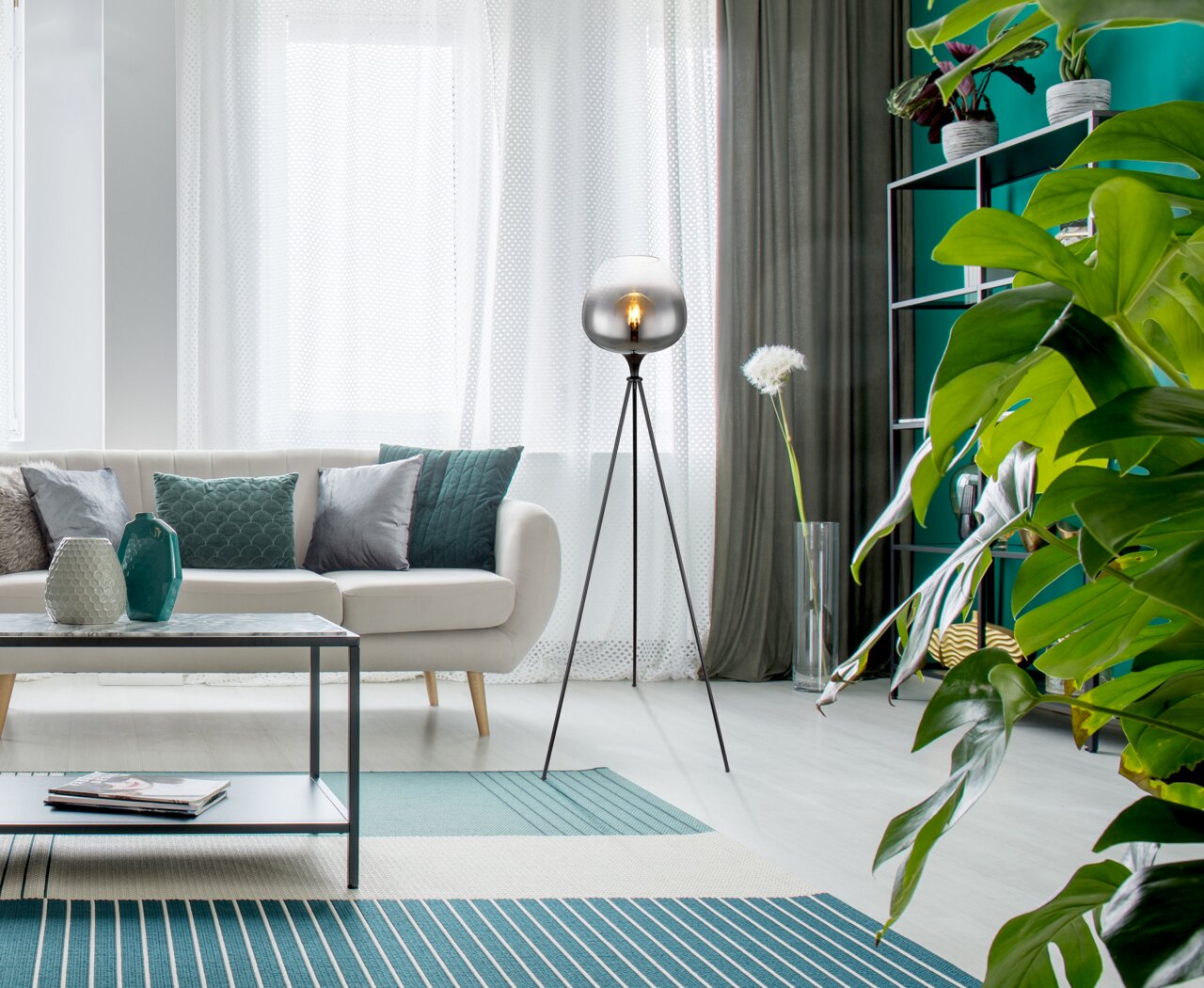 Moderne Stehleuchte MAXY mit dreibeinigem Stativ und kugelförmigem Lampenschirm in einem stilvollen Wohnzimmer, seitliche Perspektive.