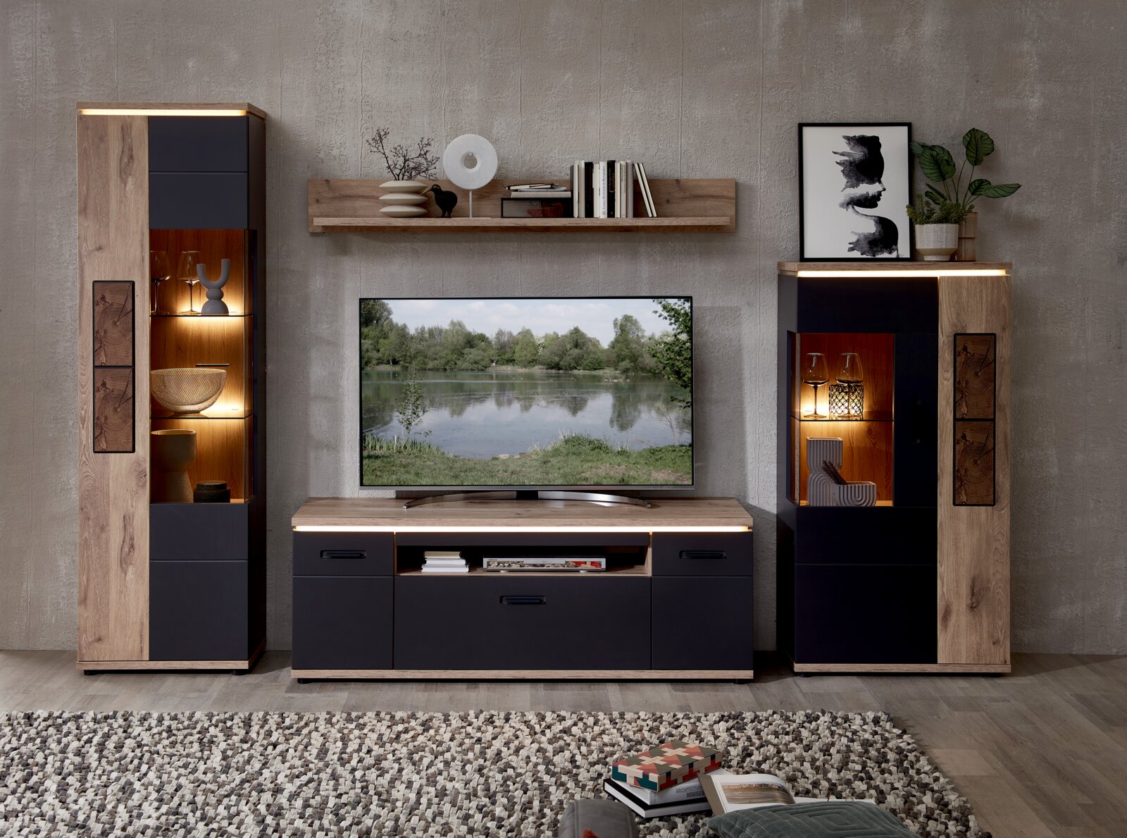 Frontale Perspektive: moderne Wohnwand im Industrial-Look mit TV-Lowboard und zwei Vitrinenschränken in Holzoptik und mattem Anthrazit, mit LED-Beleuchtung und Wandregal