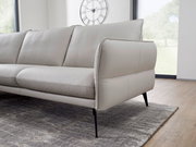 Beige Ledersofa mit schlanken schwarzen Beinen, seitliche Perspektive im modernen Wohnzimmer.