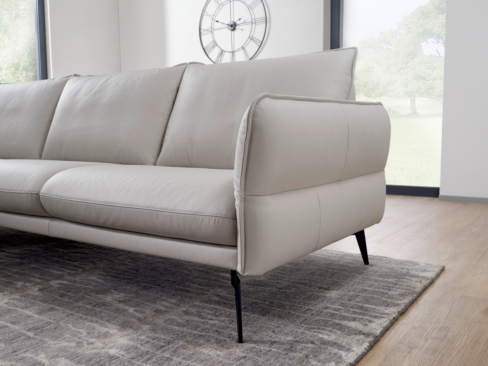 Beige leren bank met slanke zwarte poten, zijaanzicht in een moderne woonkamer.