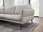 Beige leren bank met slanke zwarte poten, zijaanzicht in een moderne woonkamer.