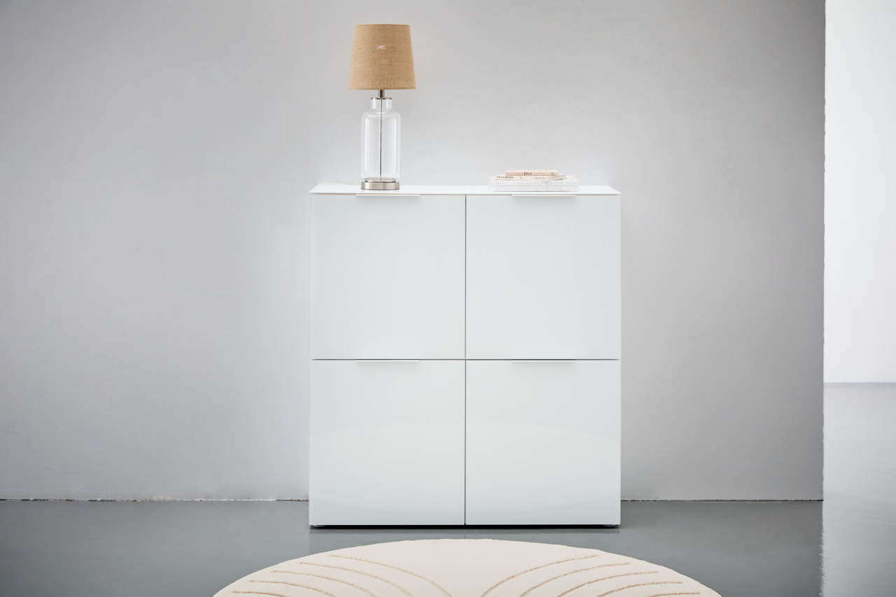 Voleo Highboard MALIN Weißes Highboard mit vier Türen, darauf eine Tischlampe und Bücher, frontale Ansicht.