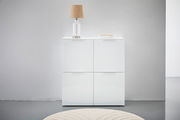 Weißes Highboard mit vier Türen, darauf eine Tischlampe und Bücher, frontale Ansicht.