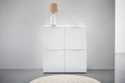 Weißes Highboard mit vier Türen, darauf eine Tischlampe und Bücher, frontale Ansicht.