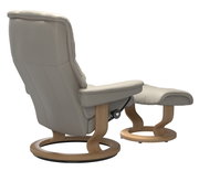 Rückansicht eines beigen Stressless Einzelsessels Mayfair mit passendem Hocker, beide mit Holzgestell.