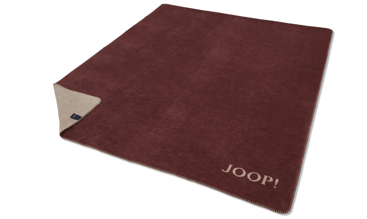 JOOP! Wohndecke MELANGE DOUBLEFACE Rote JOOP! Decke mit beiger Rückseite, ausgebreitet auf einer Fläche, mit sichtbarem Markenlogo in der Ecke.