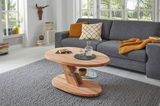 Moderner Couchtisch aus Holz mit Glasablage, in einem gemütlichen Wohnzimmer mit grauem Sofa und großen Fenstern, seitliche Perspektive.