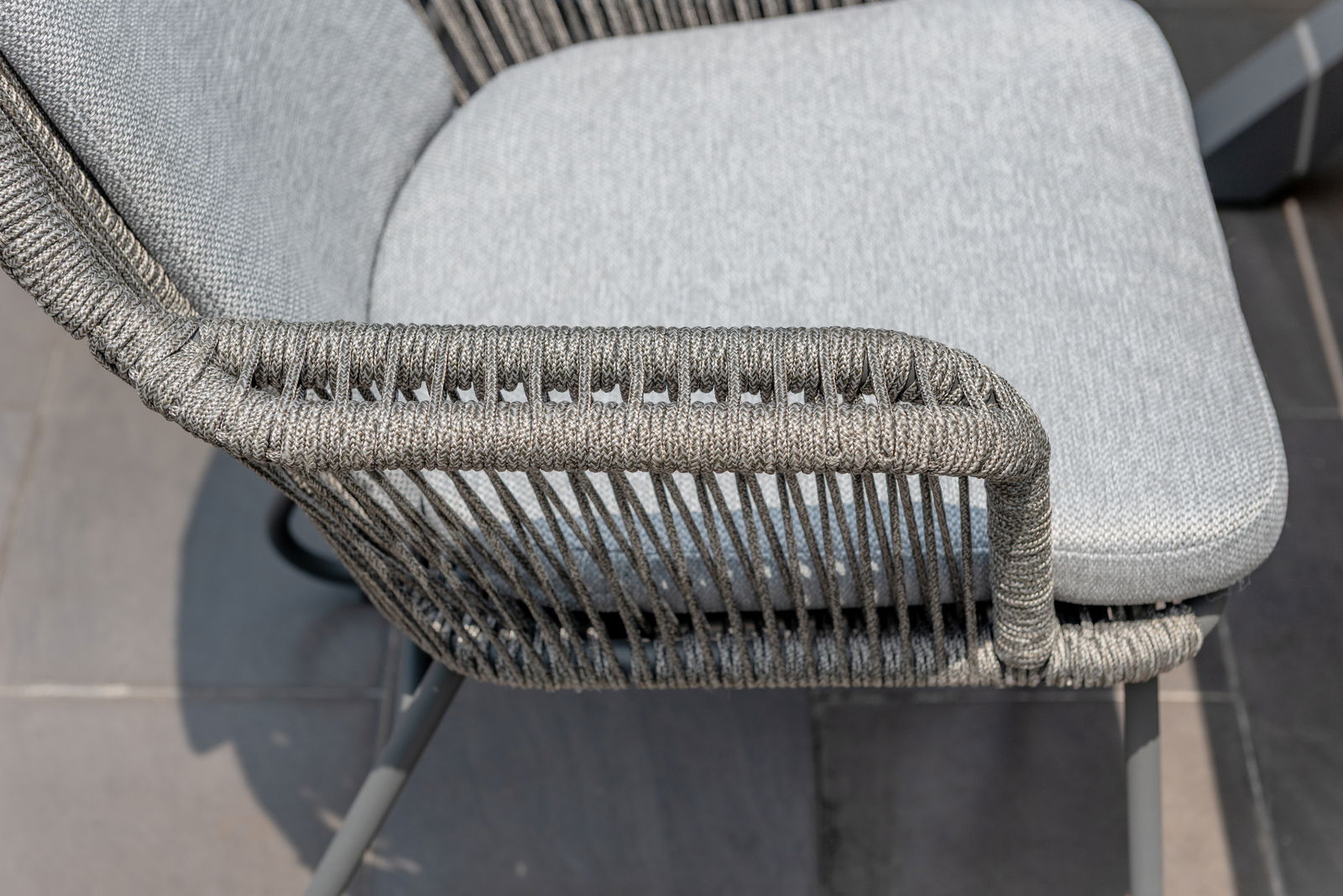 Nahaufnahme eines Armlehnstuhls mit grauem Geflecht und gepolstertem Sitz, seitliche Perspektive