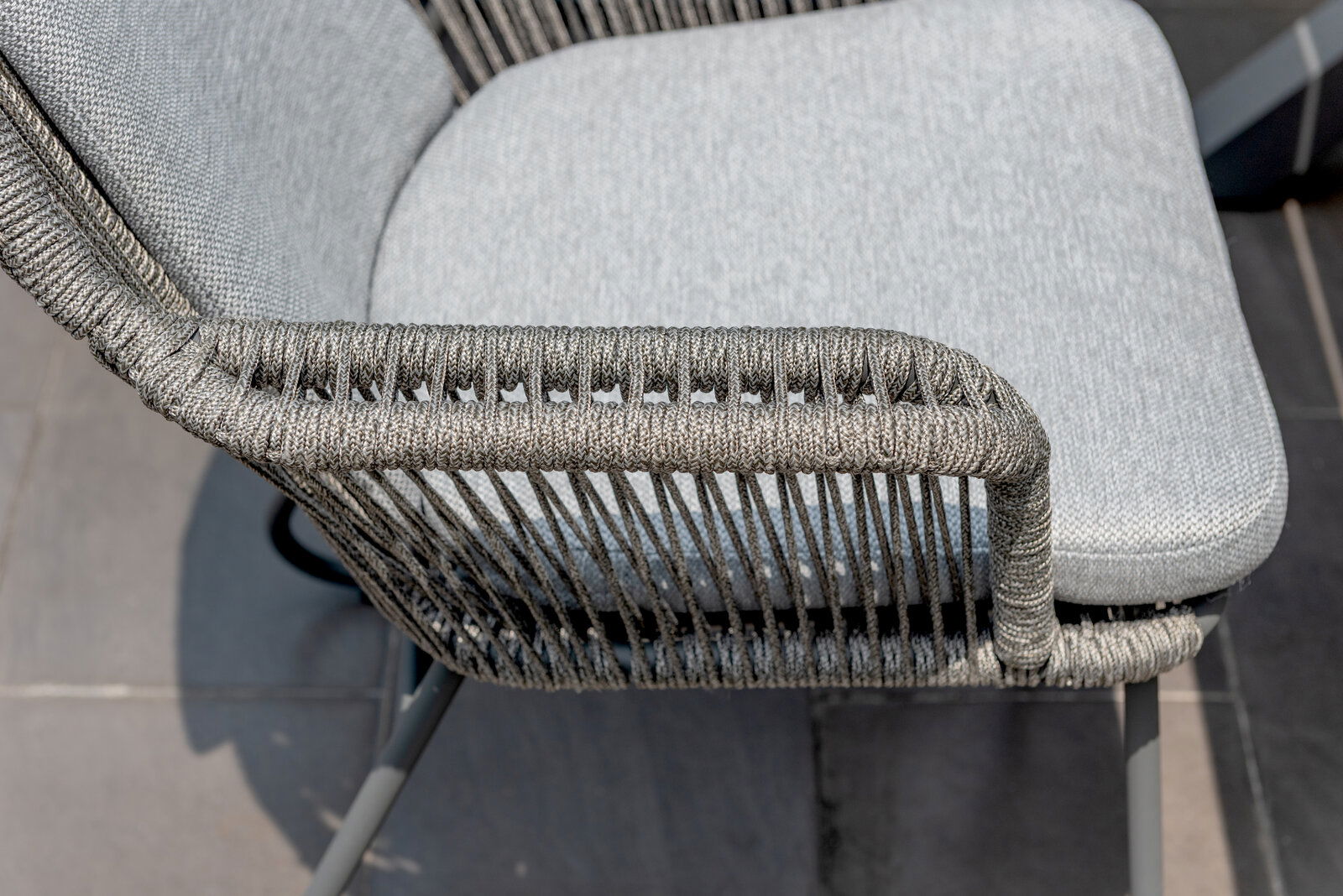 Nahaufnahme eines Armlehnstuhls mit grauem Geflecht und gepolstertem Sitz, seitliche Perspektive