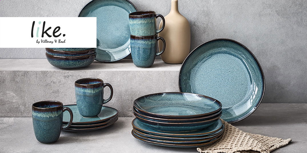 Ein stilvolles Geschirr-Set in Blaugrün mit Tellern, Schalen und Tassen auf einer grauen Fläche.