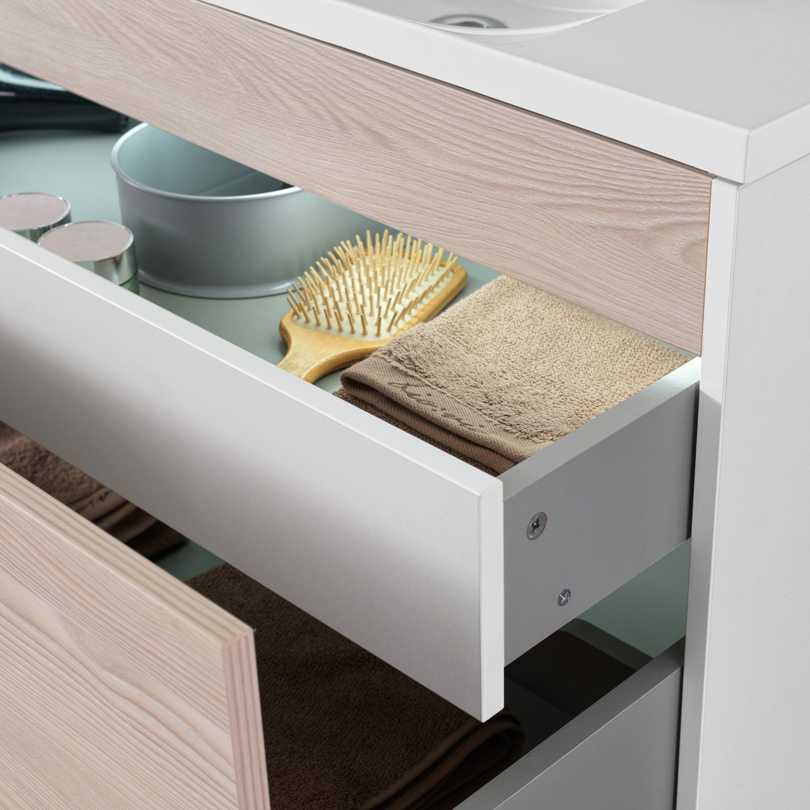 Nahaufnahme eines Waschplatzes mit geöffneten Schubladen, die Handtücher, eine Haarbürste und Dosen zeigen.