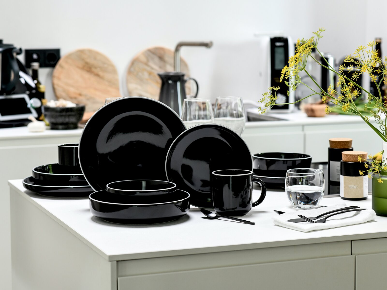 creaTable Kombiservice 10-tlg NORDIC GOURMET Schwarzes, glänzendes Geschirrset aus Tellern, Schalen und Tassen auf weißer Kücheninsel, fotografiert in leichter Schrägansicht von vorne.