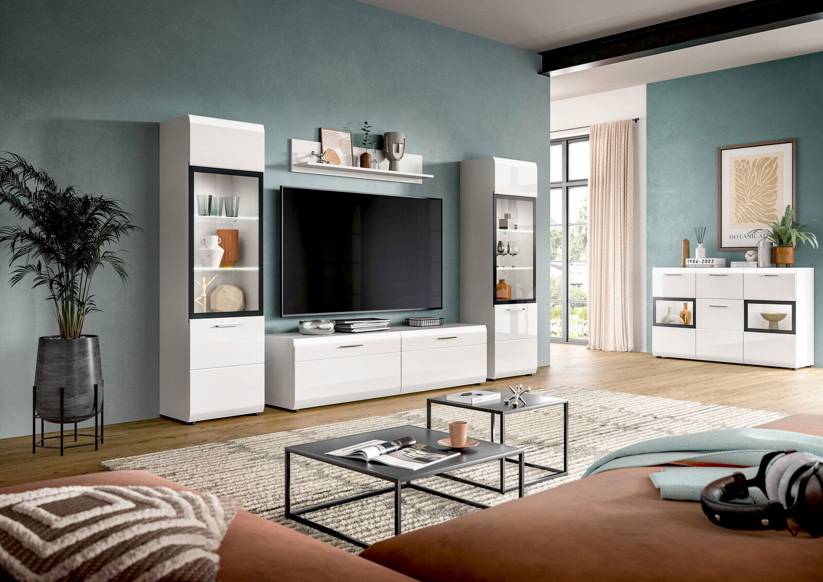 Modernes Wohnzimmer mit weißer Wohnwand: zwei hohe Vitrinen, TV-Lowboard mit großem Flachbildfernseher und Wandregal sowie passendem Sideboard, frontal in leichter Weitwinkelperspektive aufgenommen.
