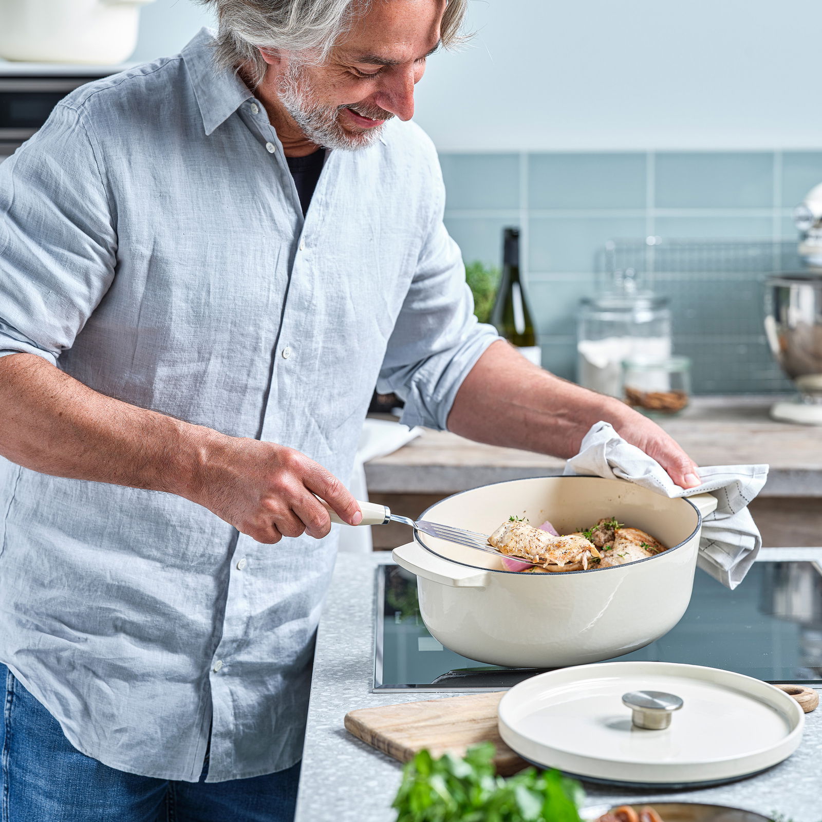 Mann kocht in einem ovalen Gusseisen Bräter von KitchenAid auf einem Herd, seitliche Perspektive.