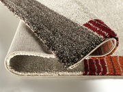 Nahaufnahme eines gefalteten Teppichs mit Streifenmuster in verschiedenen Brauntönen und Rot, Perspektive von der Seite