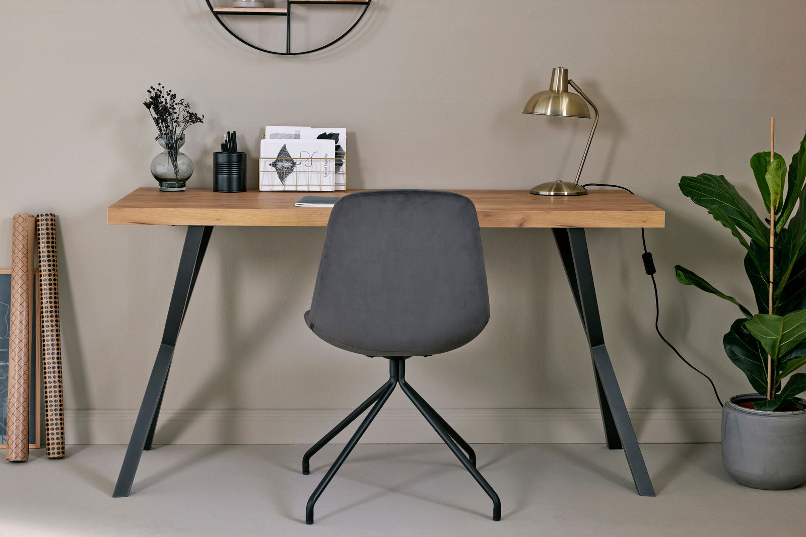 Moderner Schreibtisch mit Holzplatte und schwarzen Metallbeinen, frontal fotografiert. Dekoriert mit Lampe, Pflanzen und Schreibutensilien.