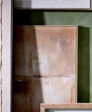 Abstract schilderij in warme beige- en bruintinten met een lichte houten lijst, vanuit vooraanzicht tegen een groene muur gefotografeerd