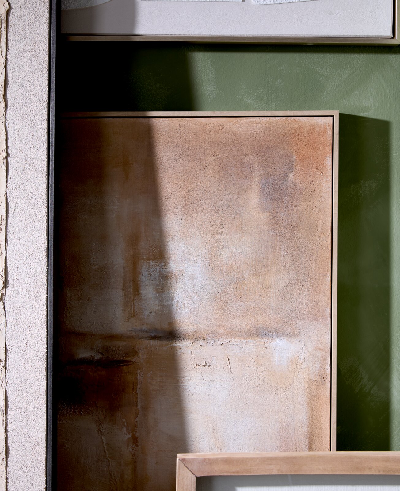Abstract schilderij in warme beige- en bruintinten met een lichte houten lijst, vanuit vooraanzicht tegen een groene muur gefotografeerd