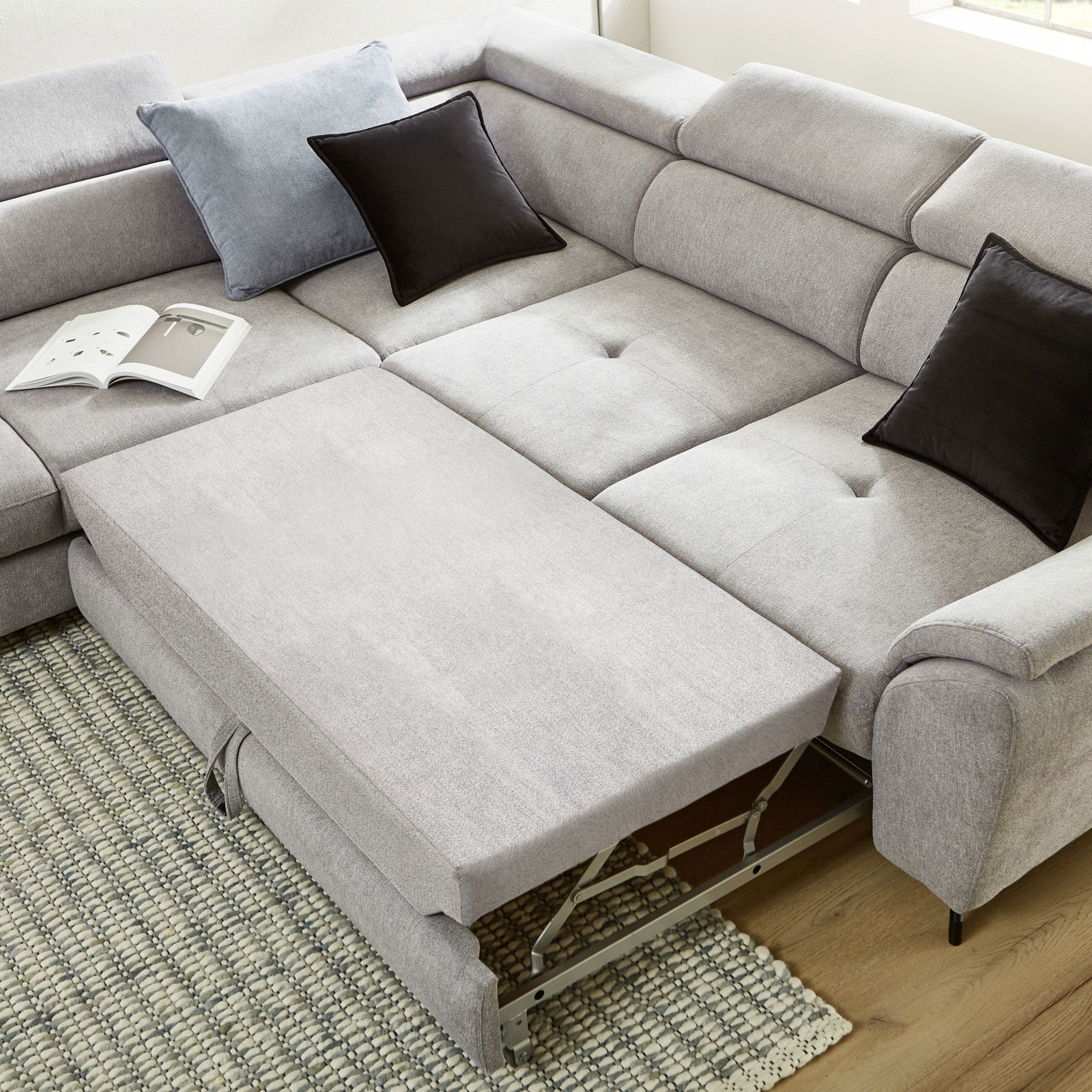 Eckgarnitur in hellem Grau mit ausziehbarem Element, von oben fotografiert, auf einem Teppich stehend, mit dekorativen Kissen.