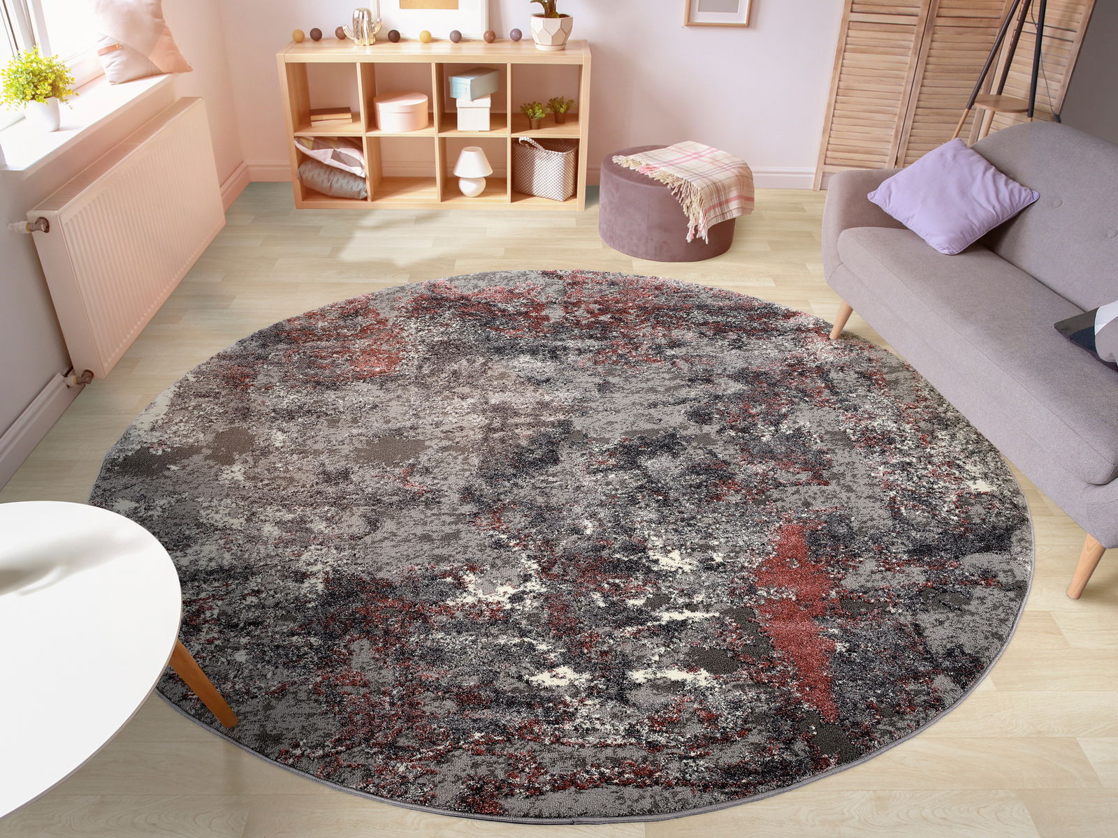 Runder Designer Teppich in einem modernen Wohnzimmer, mit abstraktem Muster in Grau- und Rottönen, aus der Vogelperspektive fotografiert.