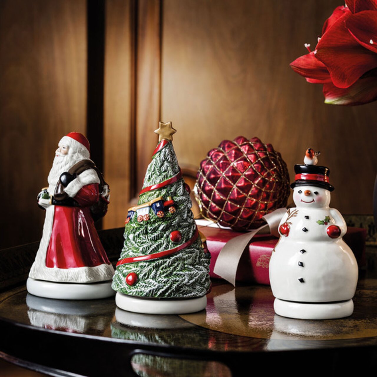 Drie kerstmuziekdoosjes op een tafel: een kerstman, een versierde kerstboom en een sneeuwpop, gezien vanuit een zijaanzicht.