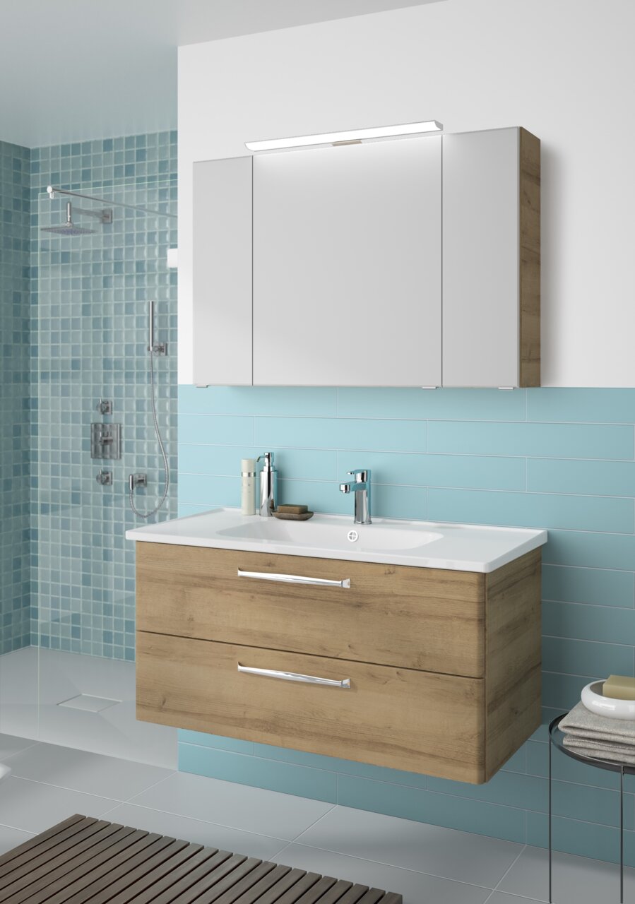 Pelipal Badblock TRENTINO Moderner Badblock mit Holzoptik und integriertem Waschbecken, frontal betrachtet. Darüber ein großer Spiegelschrank mit Beleuchtung.