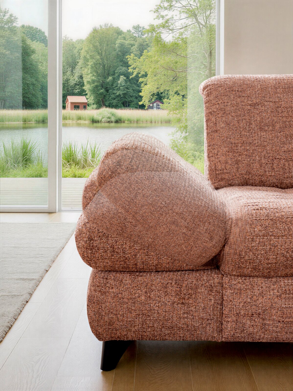 Close-up van de rechterzijde van een comfortabele bank in bruin gemêleerde bouclé stof met afgeronde armleuning en zwarte poot, gefotografeerd vanuit een licht schuine vooraanzichtperspectief bij een groot raam met uitzicht op een meer en groen bos.