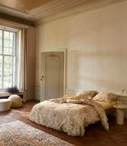 Gemütliches Schlafzimmer mit floral gemusterter Bettwäsche in einem eleganten Raum mit großen Fenstern, seitliche Perspektive.