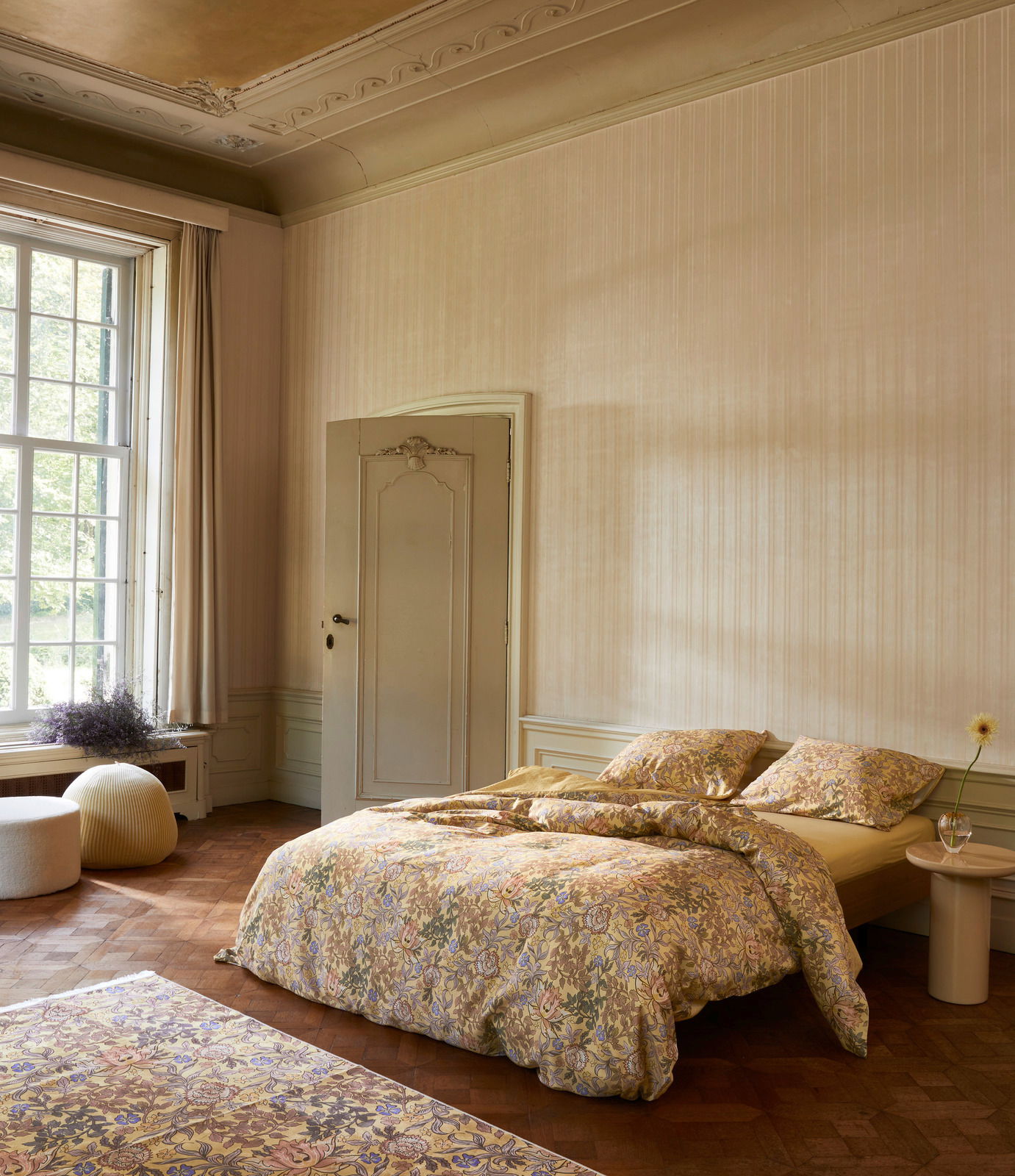 Gemütliches Schlafzimmer mit floral gemusterter Bettwäsche in einem eleganten Raum mit großen Fenstern, seitliche Perspektive.