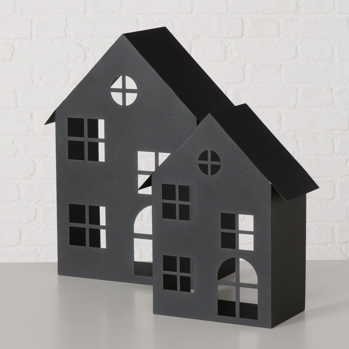 Zwei schwarze Windlichter in Form von Häusern, frontal fotografiert, mit ausgeschnittenen Fenstern und Türen, auf einem hellen Hintergrund.