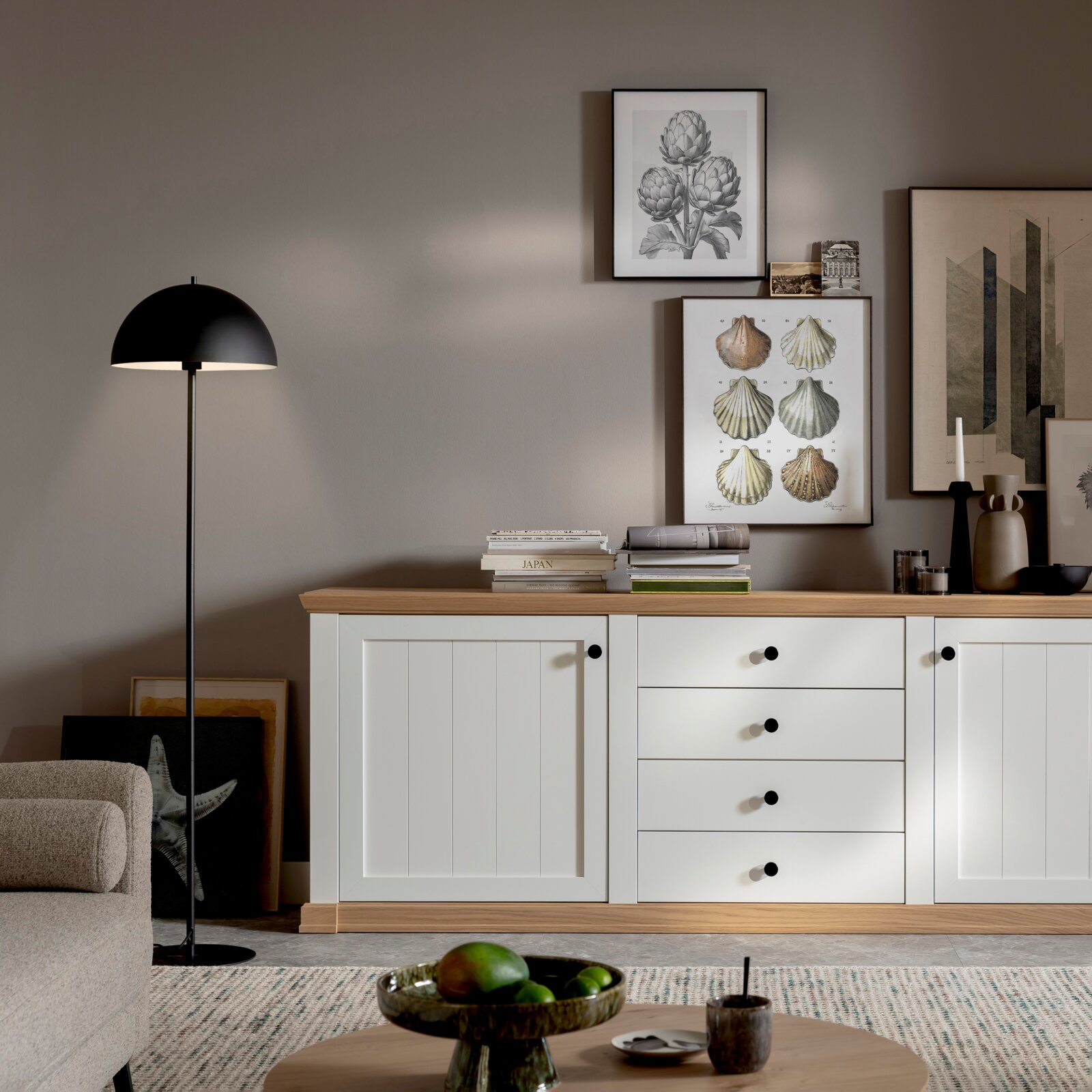 Skandinavisches Sideboard in Weiß mit Eichenholzplatte und schwarzen Knöpfen, im Wohnzimmer mit Bilderwand und schwarzer Stehleuchte, Frontansicht auf Augenhöhe