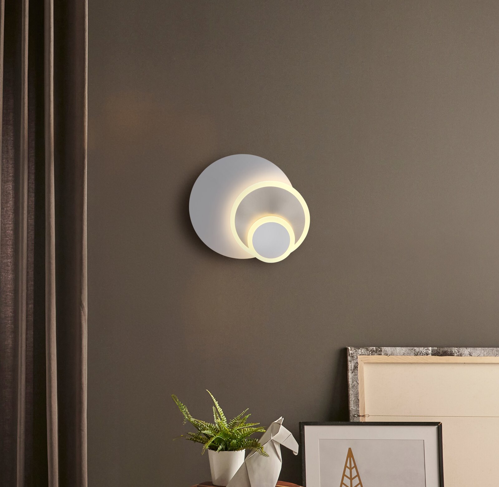 Moderne LED-Wandleuchte in Weiß mit zwei leuchtenden, überlappenden Ringen an einer grauen Wand, Frontansicht leicht von rechts.