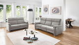 Graues 2,5er Sofa in einem modernen Wohnzimmer mit großen Fenstern, Holzboden und stilvollen Dekorationen, seitliche Perspektive.