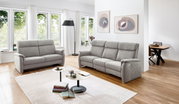 Graues 2,5er Sofa in einem modernen Wohnzimmer mit großen Fenstern, Holzboden und stilvollen Dekorationen, seitliche Perspektive.